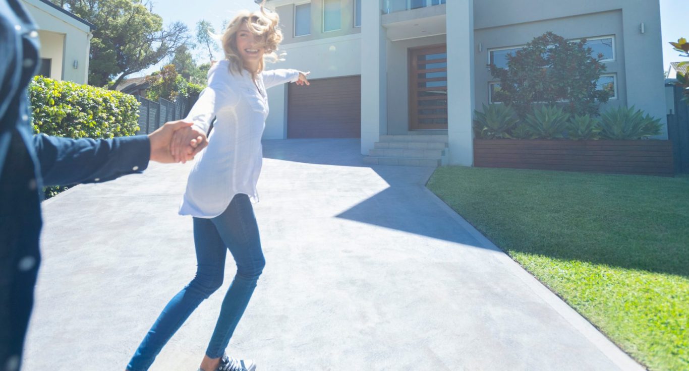 Junge Frau läuft lächelnd auf ein modernes Haus zu, während sie an der Hand gehalten wird.