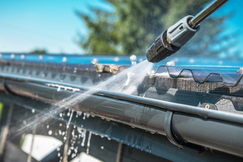 Wasserstrahl reinigt die Dachrinne unter klarem Himmel.
