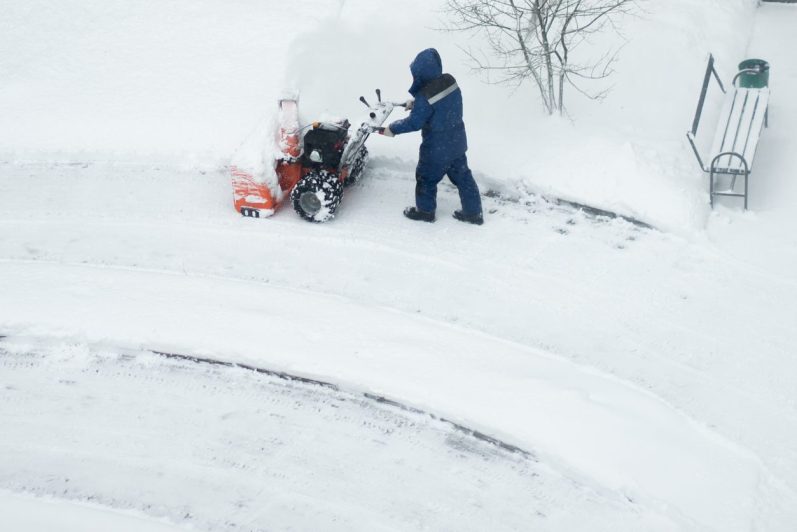 Eine Person in blauer Arbeitskleidung räumt Schnee mit einem Schneepflug.